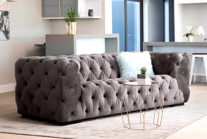 Velvet grey, buttoned couch on light grey rug in modern living room 